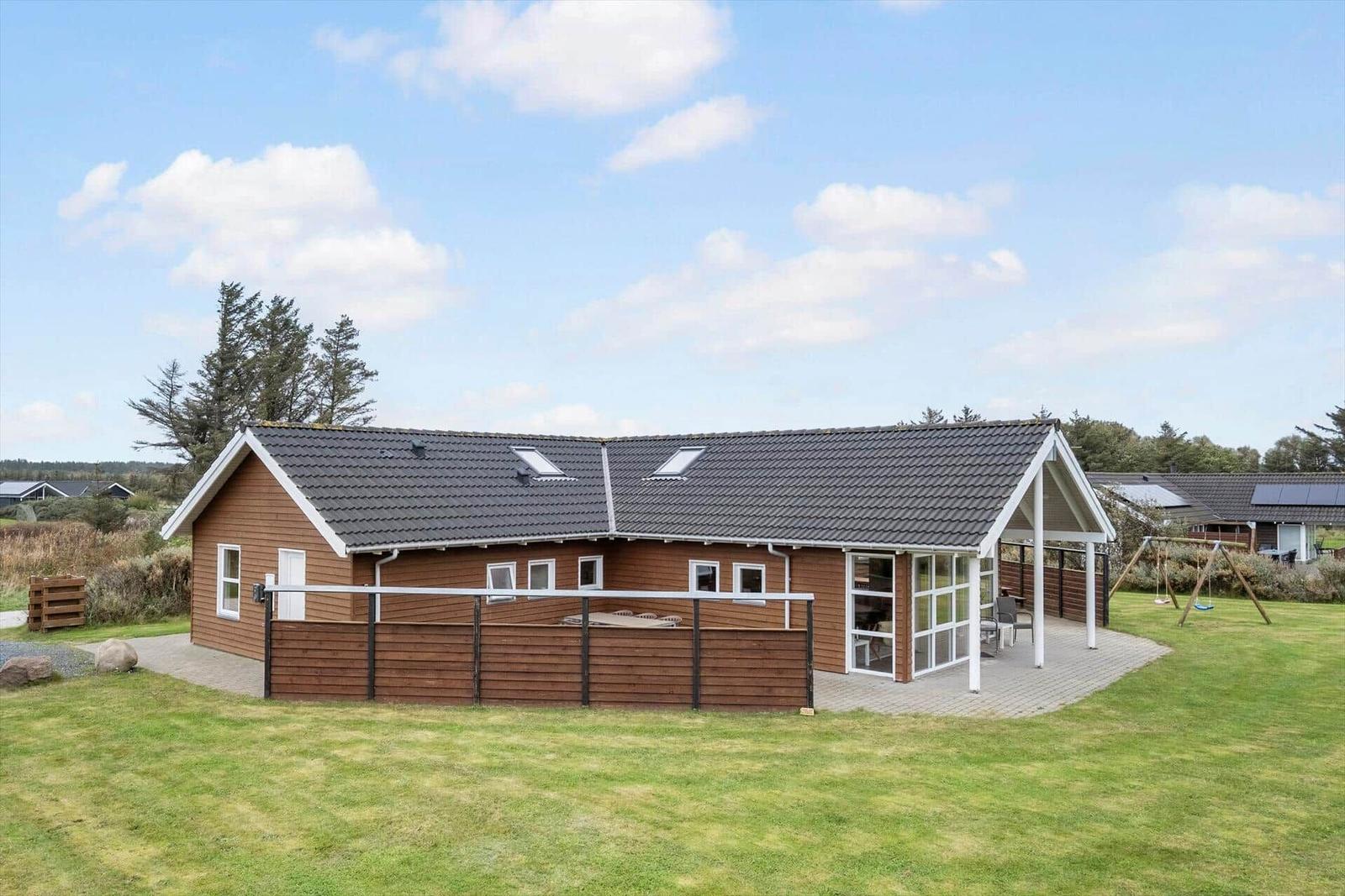 Wooden house with terrace and garden. Playground in the background.