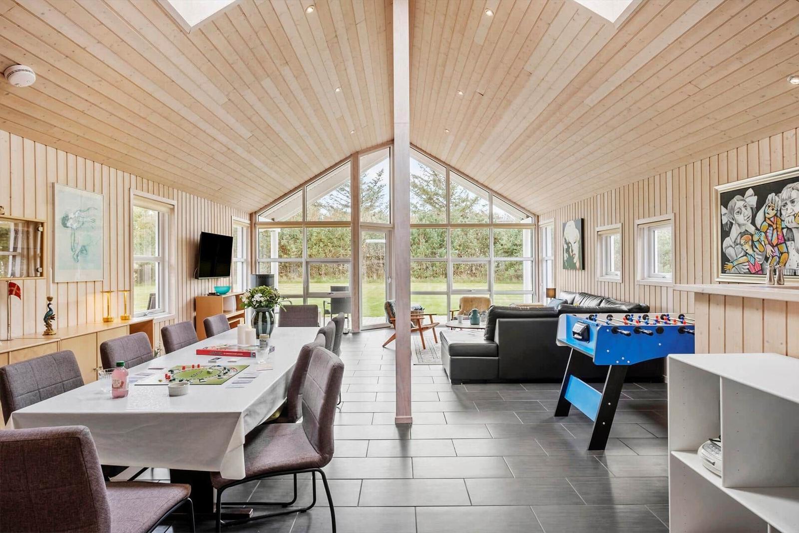 Large space with dining area, sofa, and foosball table. Wooden ceiling and large windows.