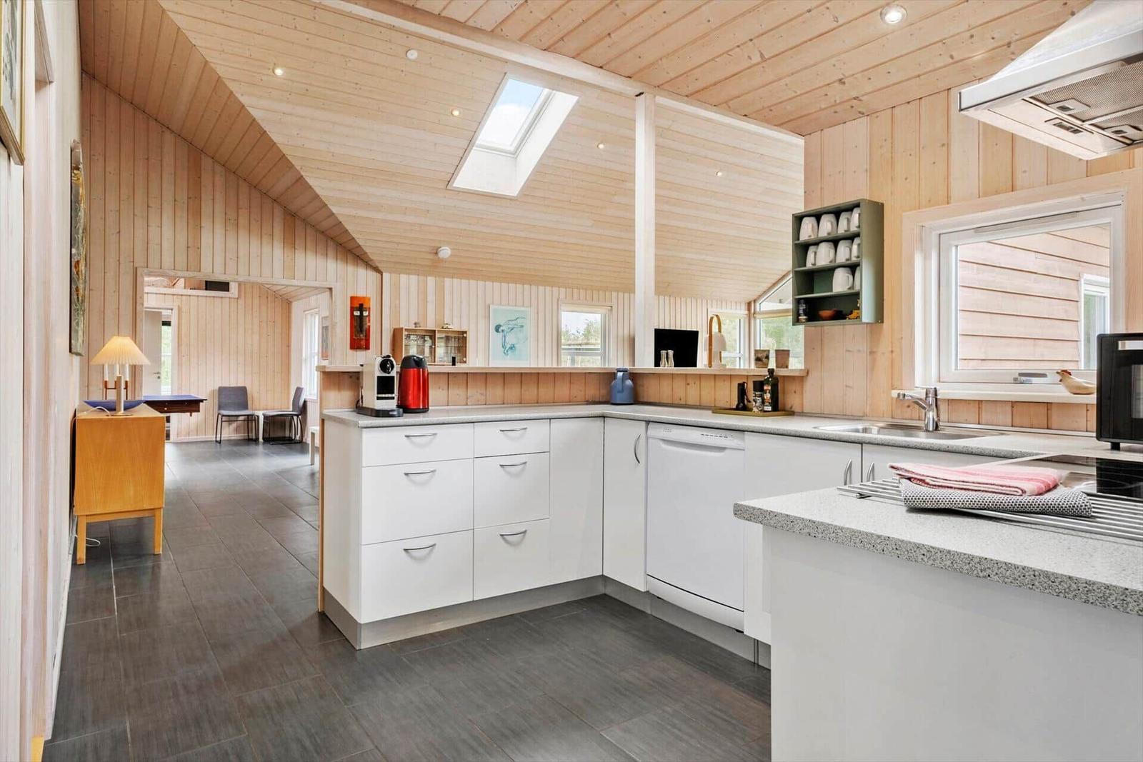 Kitchen with white cabinets, granite countertop, and wood walls. Skylight and windows provide daylight.