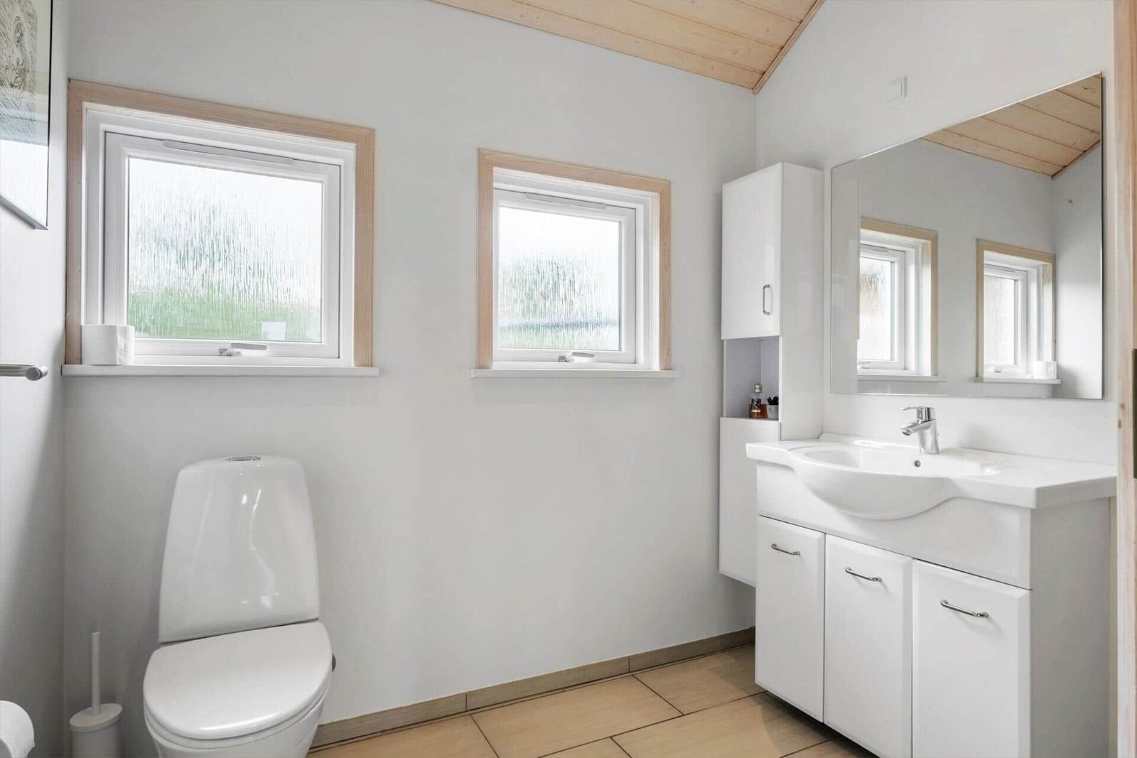 Bathroom with toilet, sink, and two windows with wooden frames.