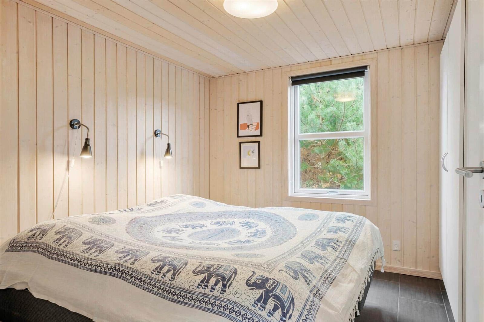 Bedroom with wooden walls, bed with elephant blanket, and window overlooking trees.