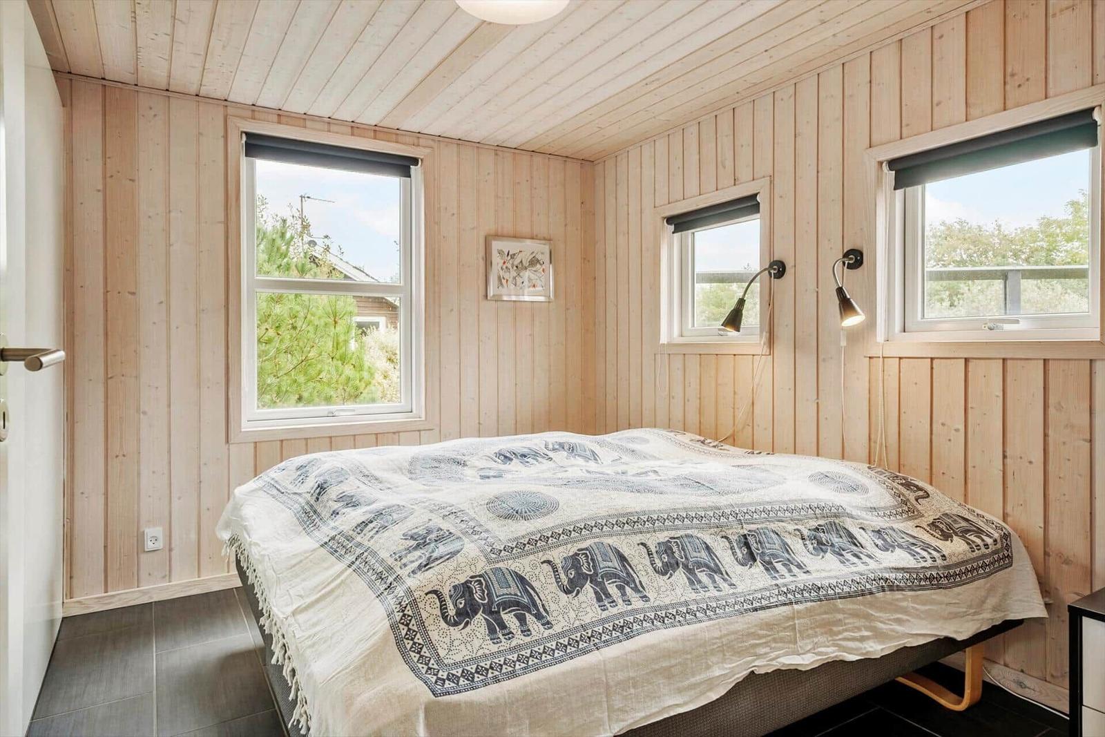 Bedroom with wooden walls, bed with elephant blanket, and two windows.