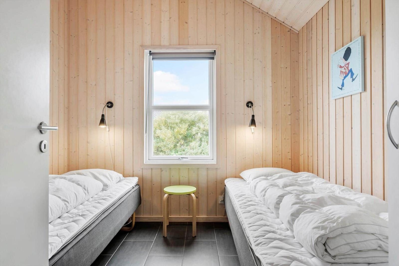 Two single beds, window with view of green, wooden walls and stool.