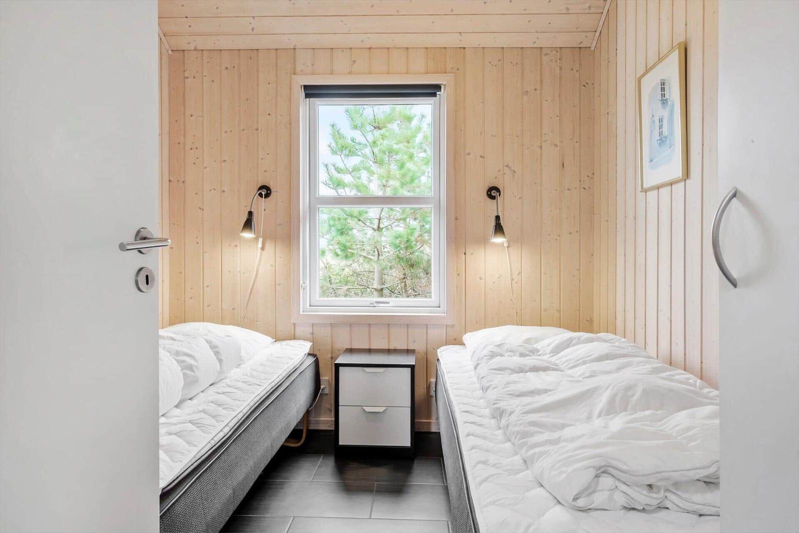 Two beds with white bedding, wooden walls, and window with view of trees.