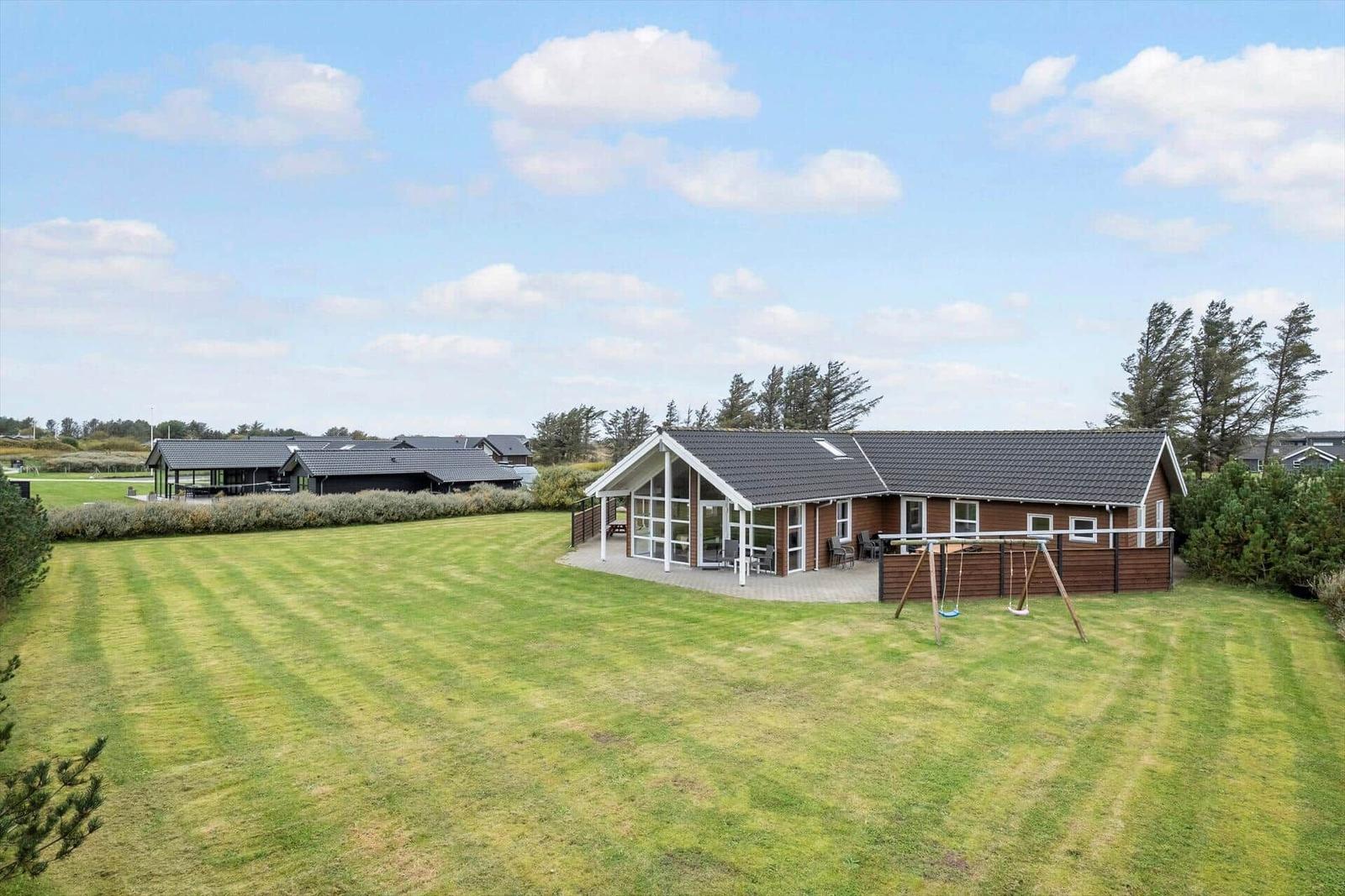 Wooden house with large garden and playground under blue sky.