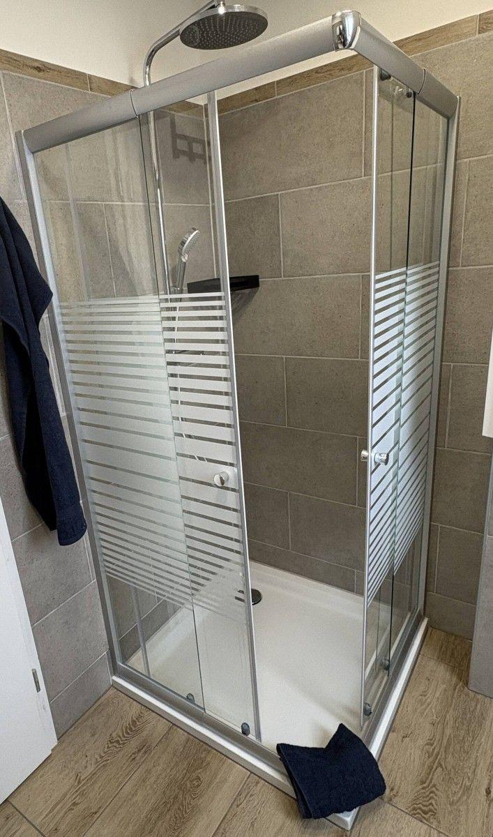 Shower cabin with glass door and showerhead. Floor and walls are tiled.