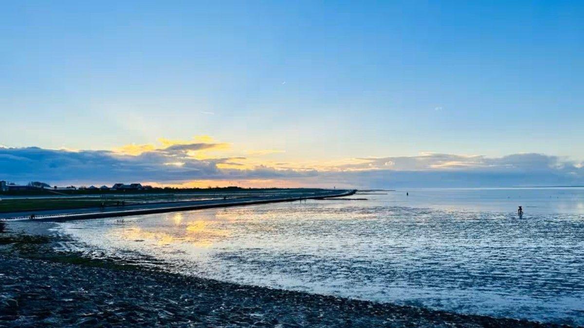 Sunset over water with sloping beach and reflections on the surface.