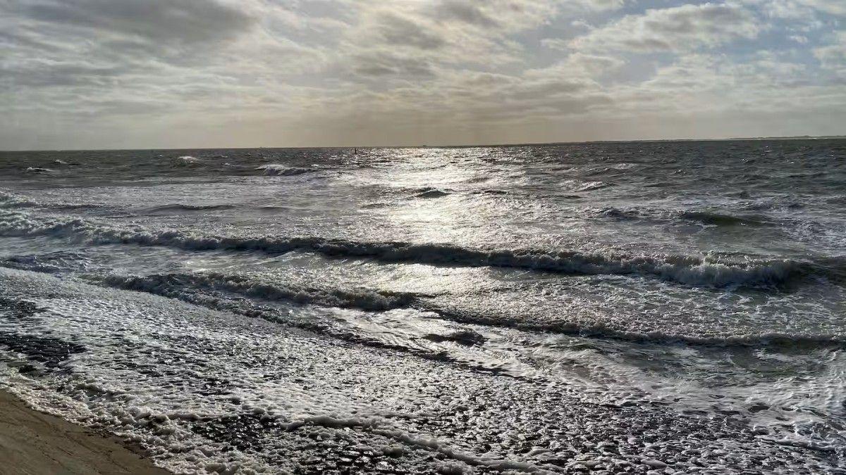 Waves break on a sandy beach under a cloudy sky.