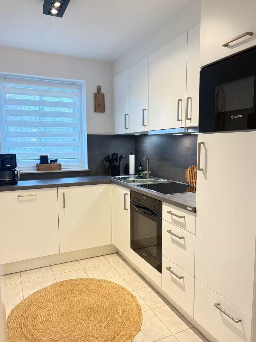 Kitchen with white cabinets, stainless steel appliances, and round jute rug.