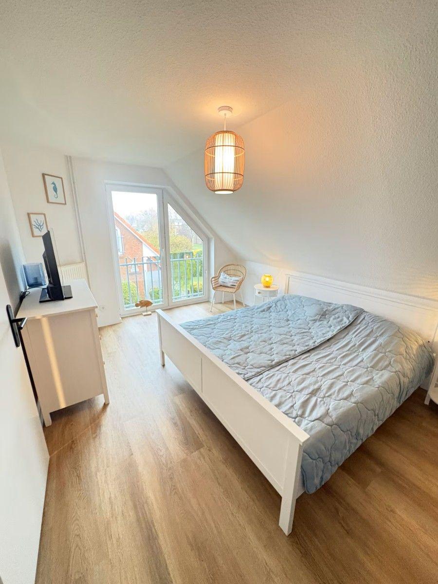 Bedroom with sloped ceiling, bed, TV stand, and balcony door.