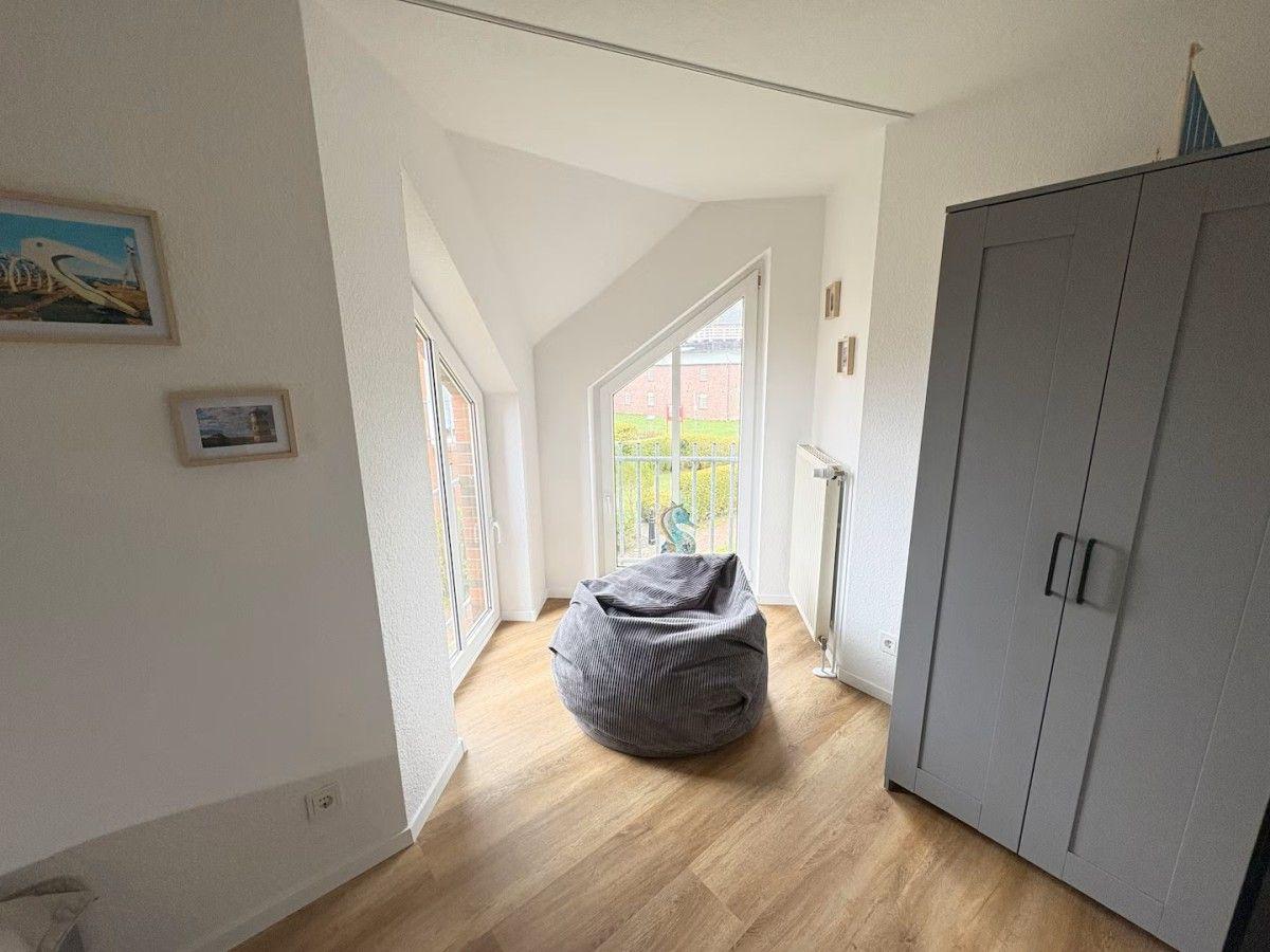 Room with gray bean bag, wooden floor, and large window with view.
