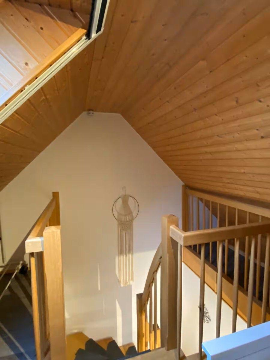 Wood-paneled ceiling and staircase with handrail. A macrame object hangs on the wall.