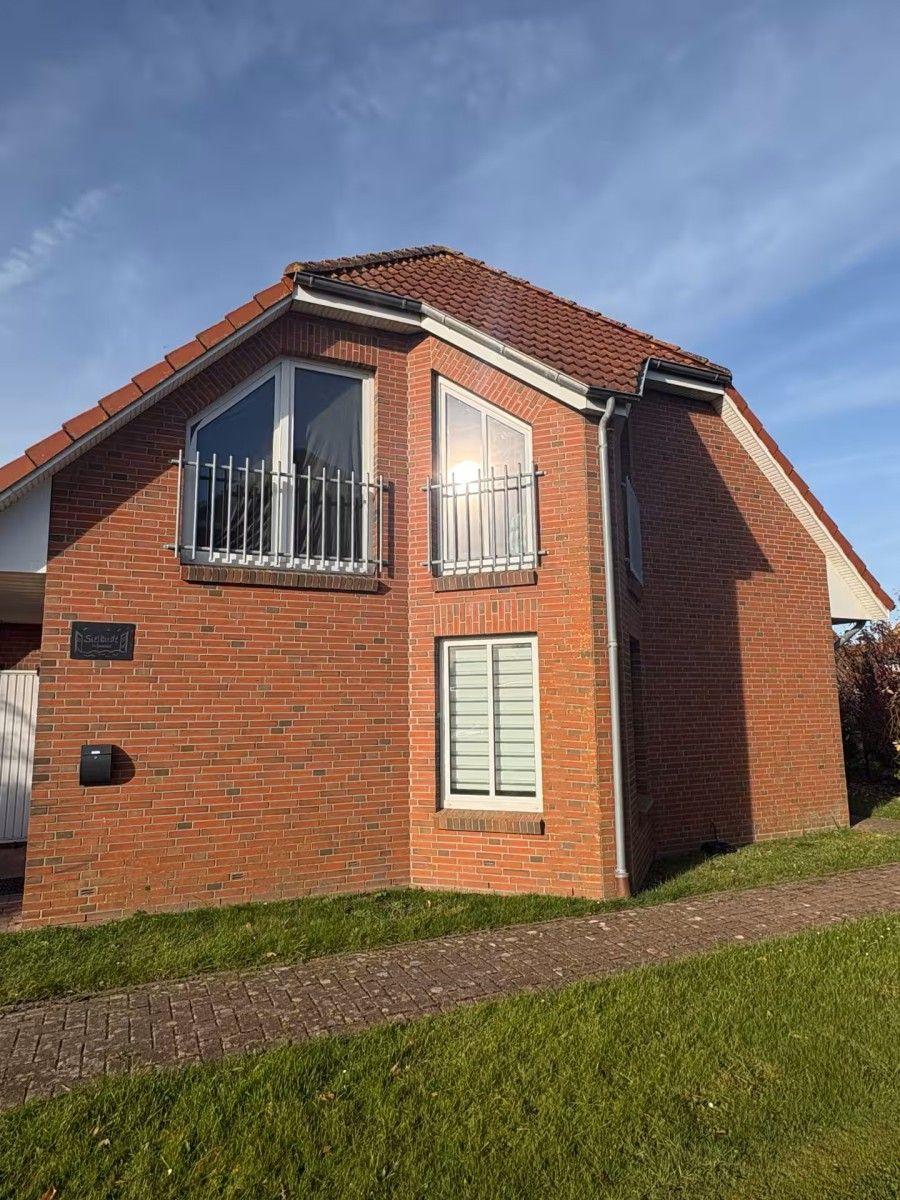 Two-story house with red tiled roof and balcony. Green lawns and paved paths.