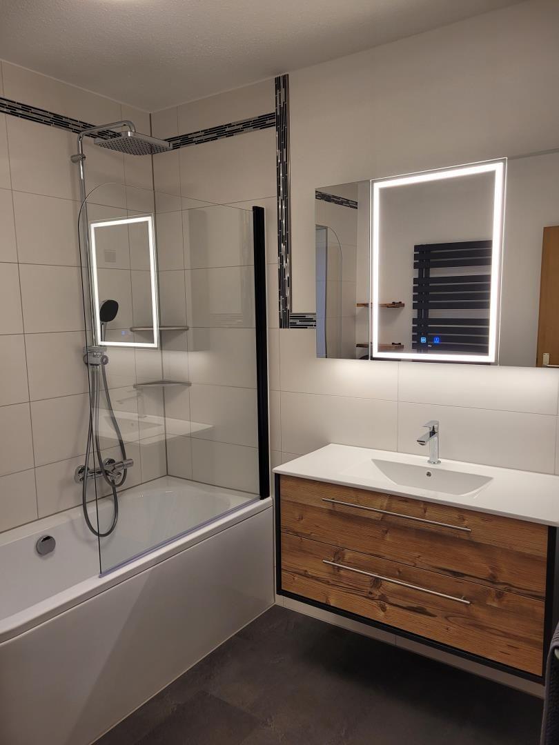 Bathroom with shower, sink, and illuminated mirror.