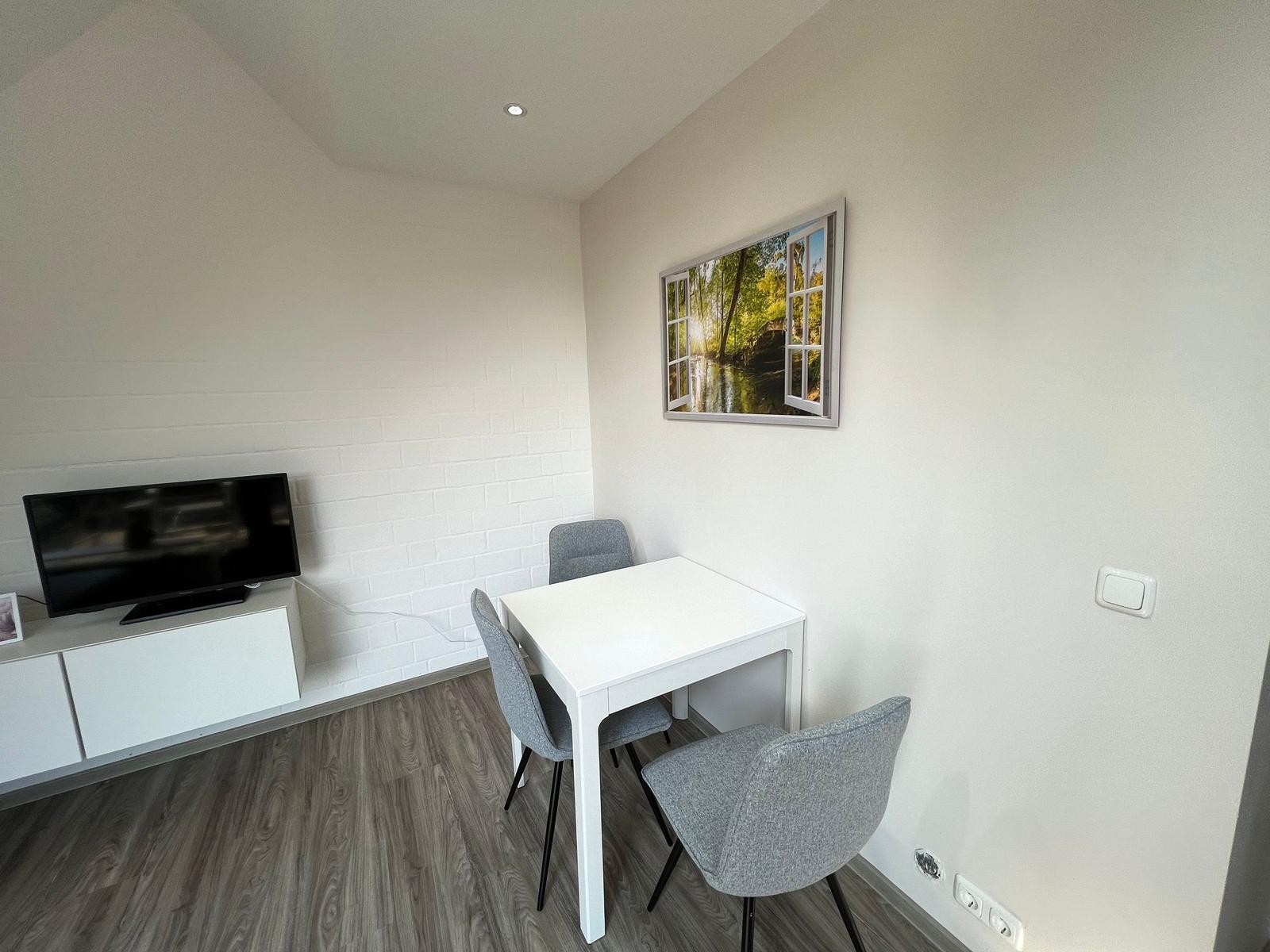 Kleiner Raum mit Tisch, Stühlen, Fernseher und Wandbild.