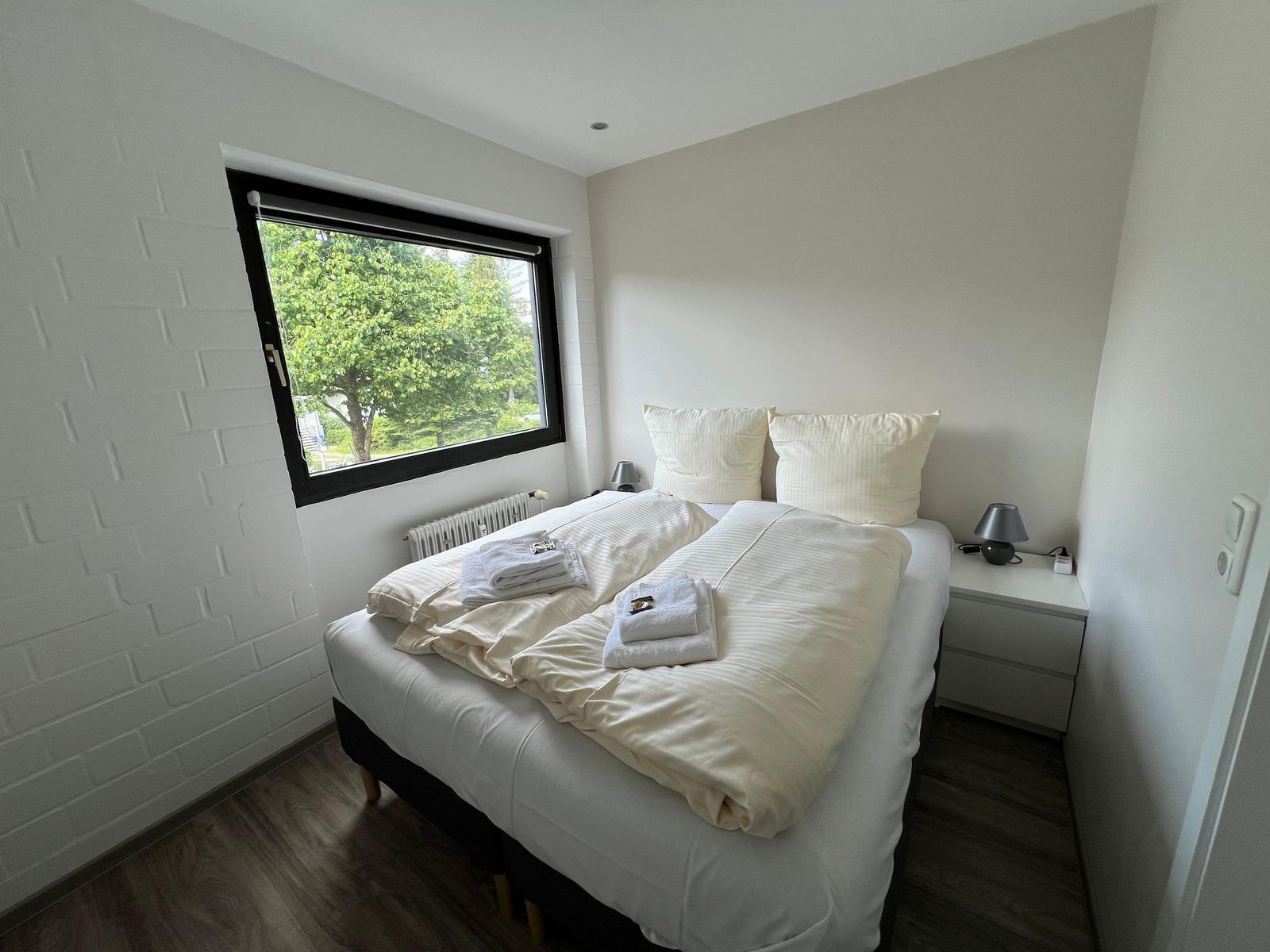 Schlafzimmer mit Doppelbett, Fenster und Nachttisch.