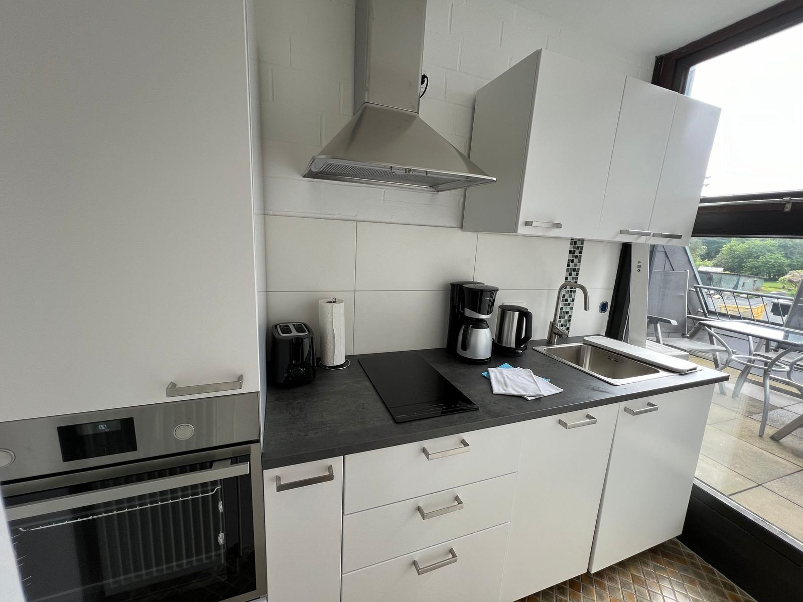 Küche mit weißen Schränken, Induktionskochfeld und Blick auf Balkon.