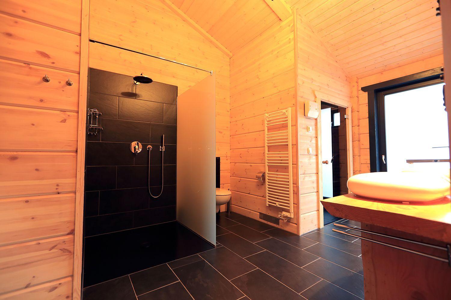 Badezimmer mit Dusche, Waschbecken und Heizkörper an Holzwand