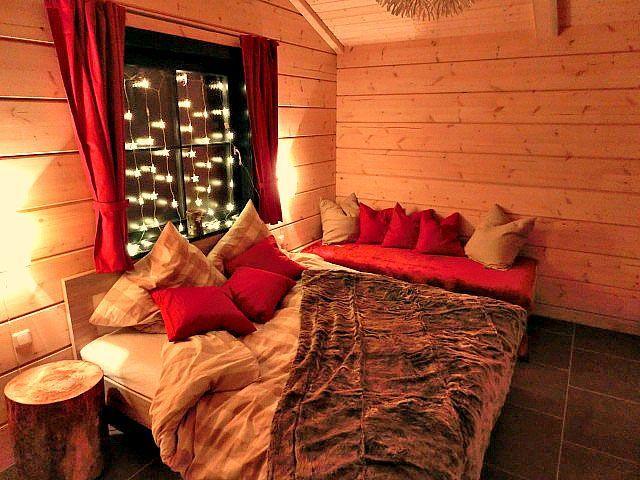 Schlafzimmer mit Holzwand, Bett, roten Kissen und Fenster mit Lichterkette.