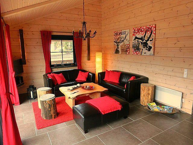 Wohnzimmer mit Holzwänden, zwei schwarzen Sofas, rotem Teppich und Holztisch.