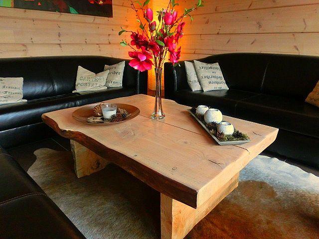 Ein Wohnzimmer mit schwarzen Sofas, einem rustikalen Holztisch und einer Blumenvase.