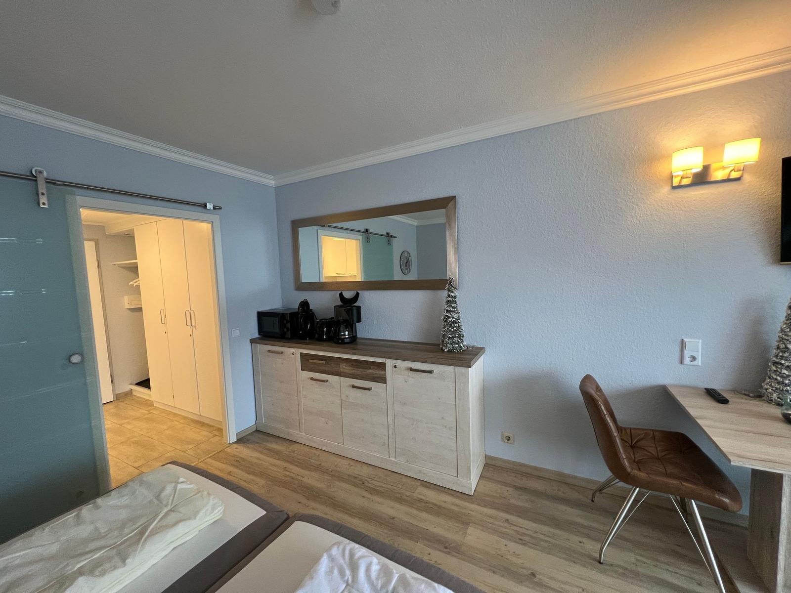 Schlafzimmer mit Schreibtisch, Spiegelschrank und Kleiderschrank im Hintergrund.