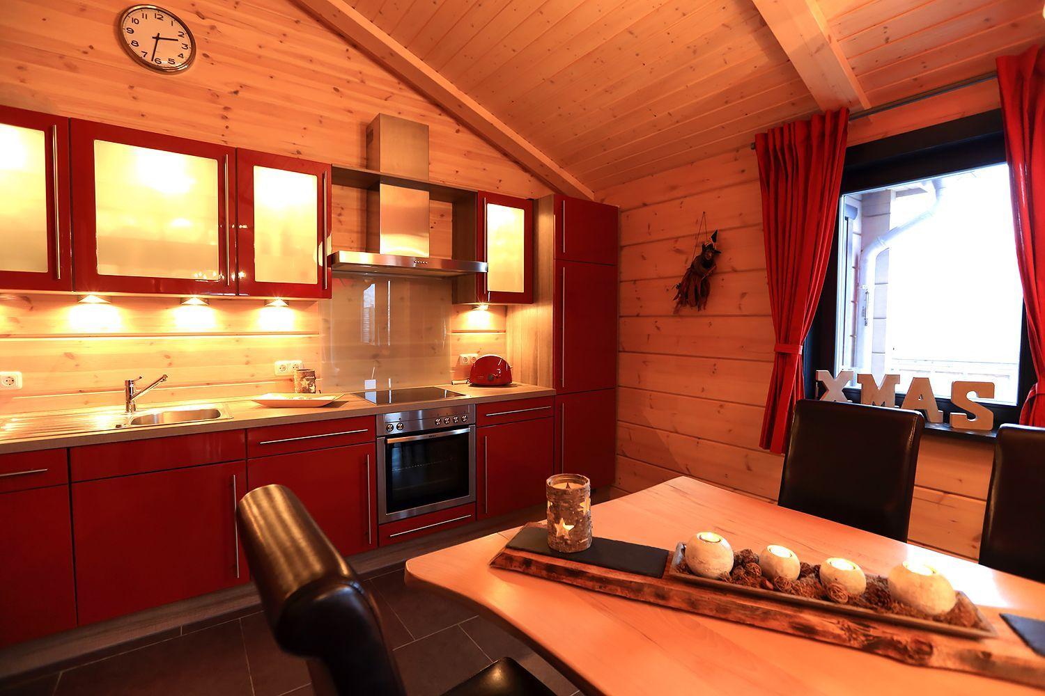 Küche mit roten Schränken, Holzwand und Esstisch mit Kerzen.
