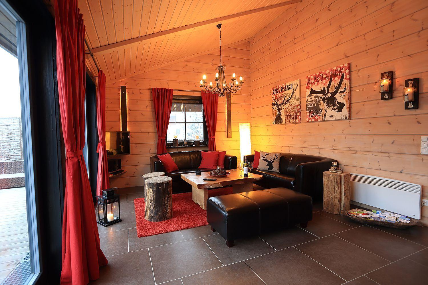 Wohnzimmer mit Holzwand, roten Vorhängen und Ledersofa. Es gibt einen Holztisch und einen Kamin.