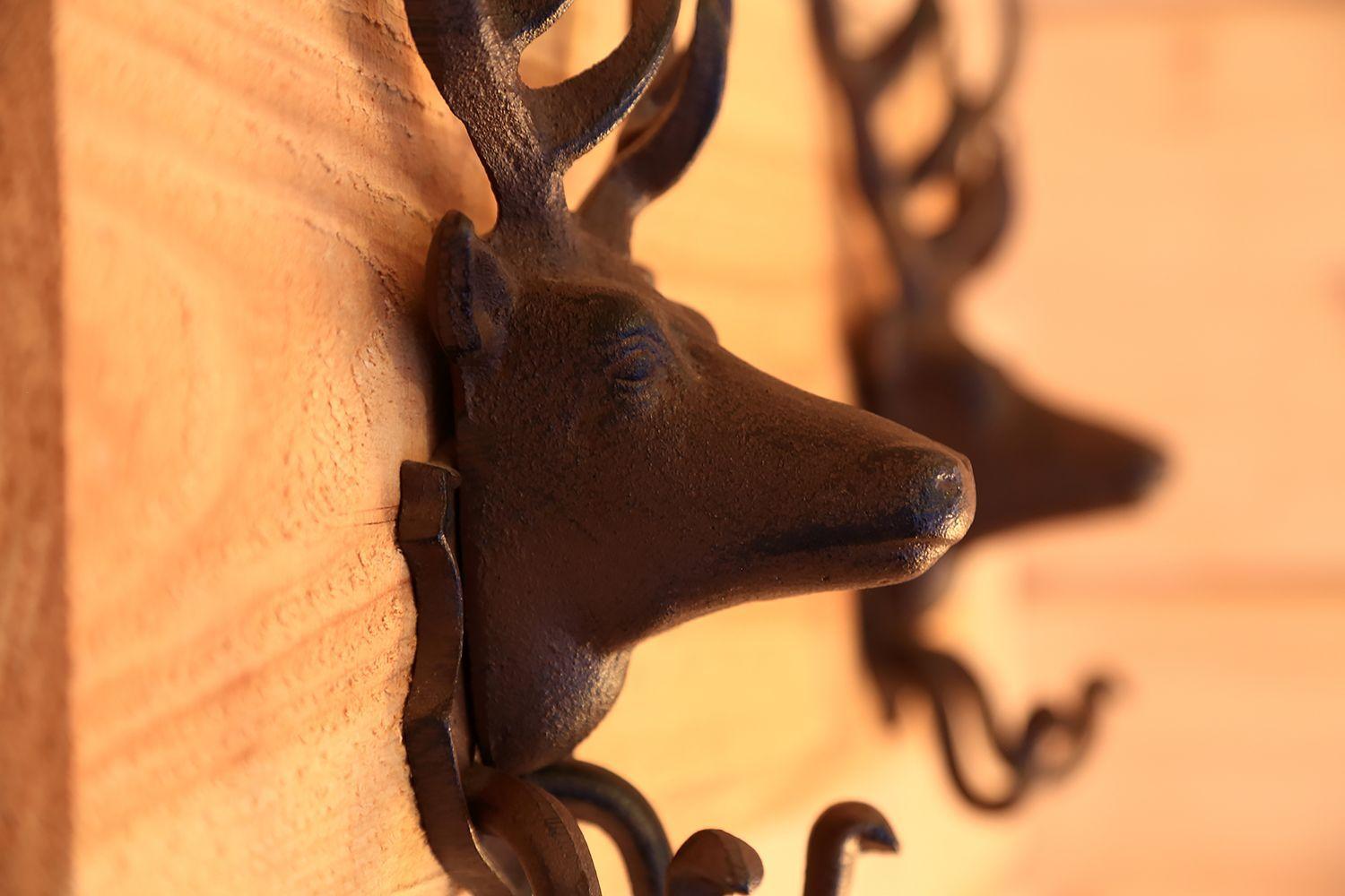 Metallhaken in Form von Hirschköpfen an einer Holzwand montiert.