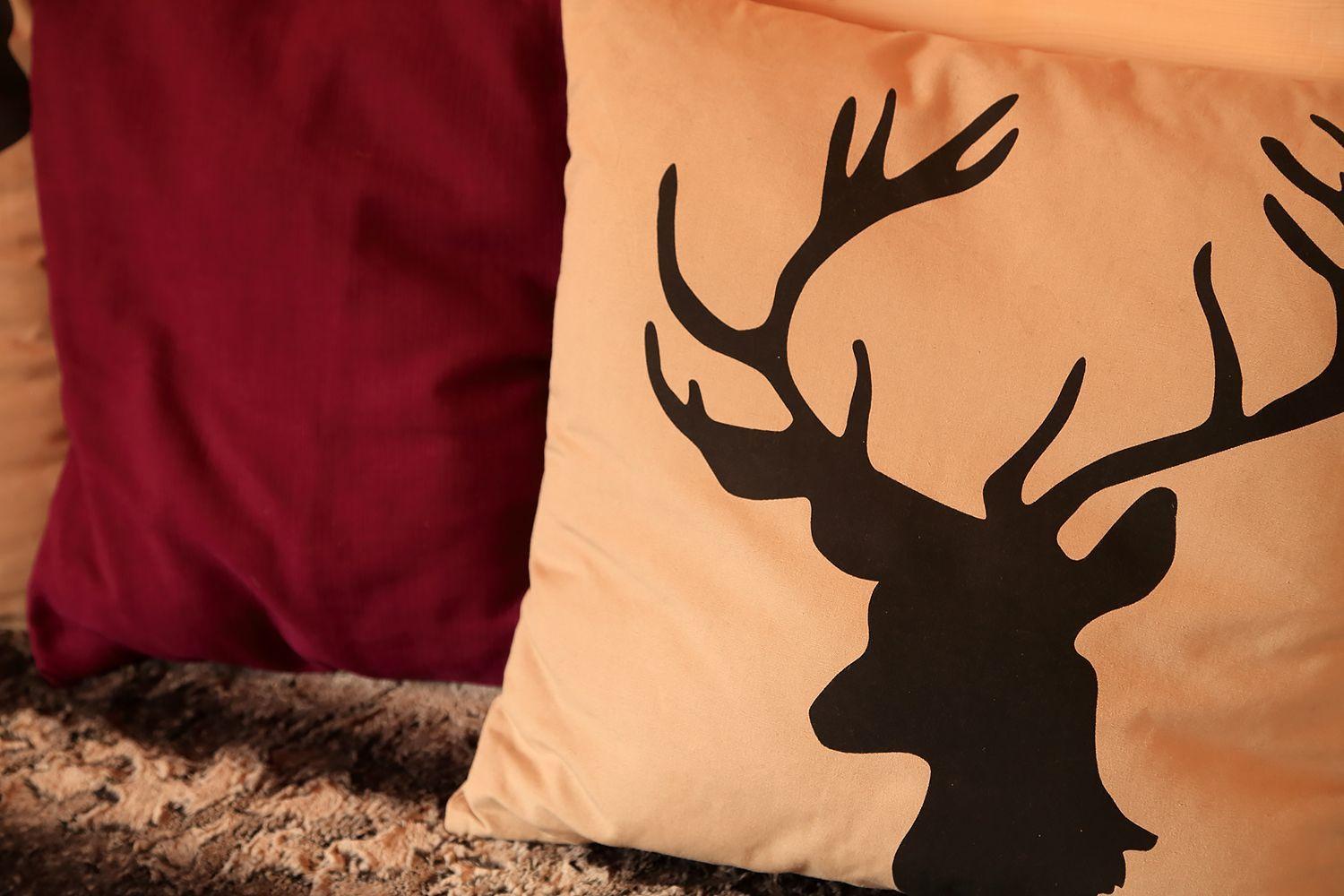 Kissen mit Hirschsilhouette neben einem roten Kissen auf einem Teppich.
