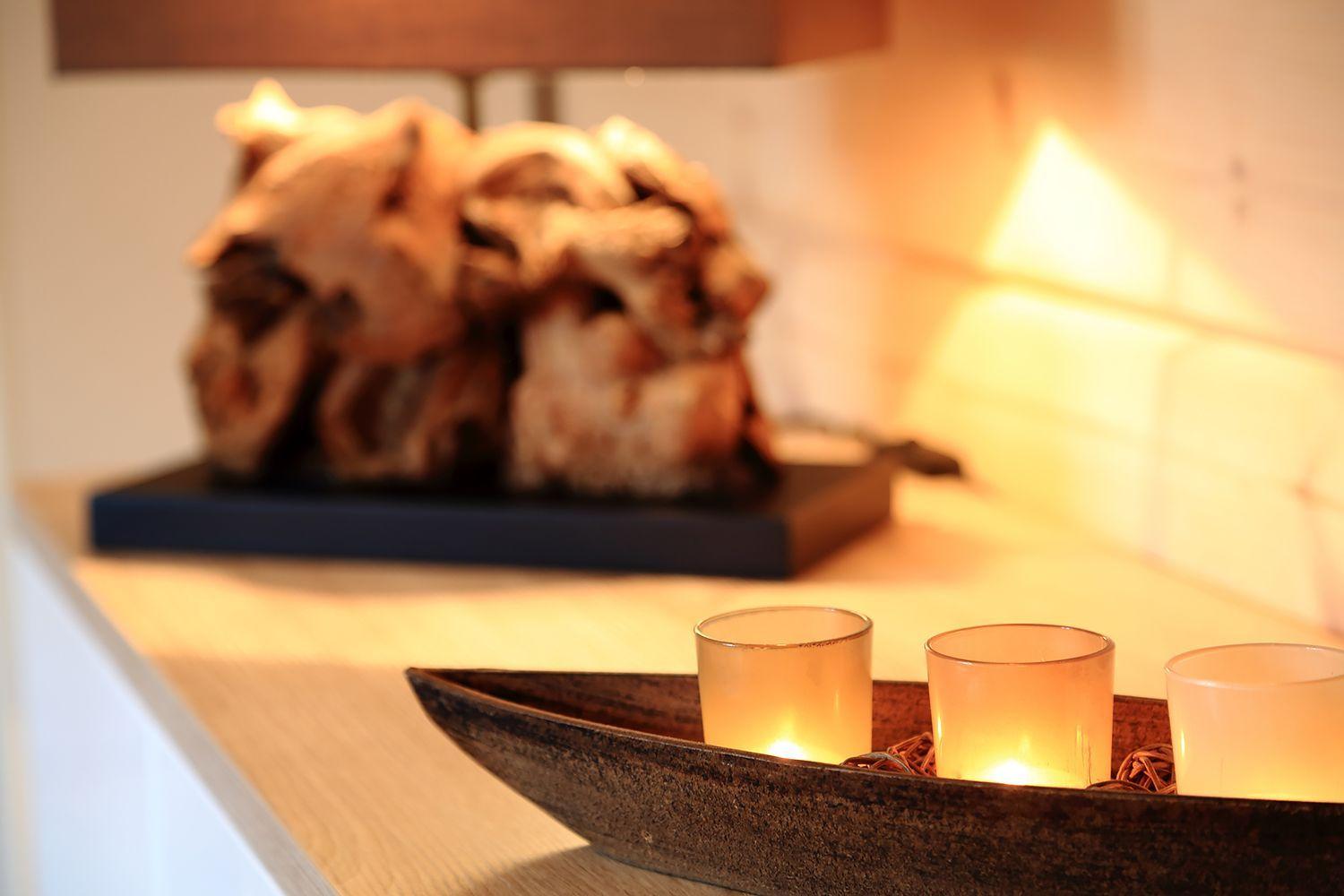Drei brennende Kerzen in einem Boot auf einer Holzoberfläche vor einer Skulptur.