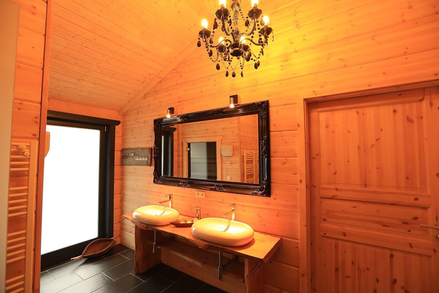 Badezimmer mit zwei Waschbecken, Spiegel und Kronleuchter. Holzwände und -decke.