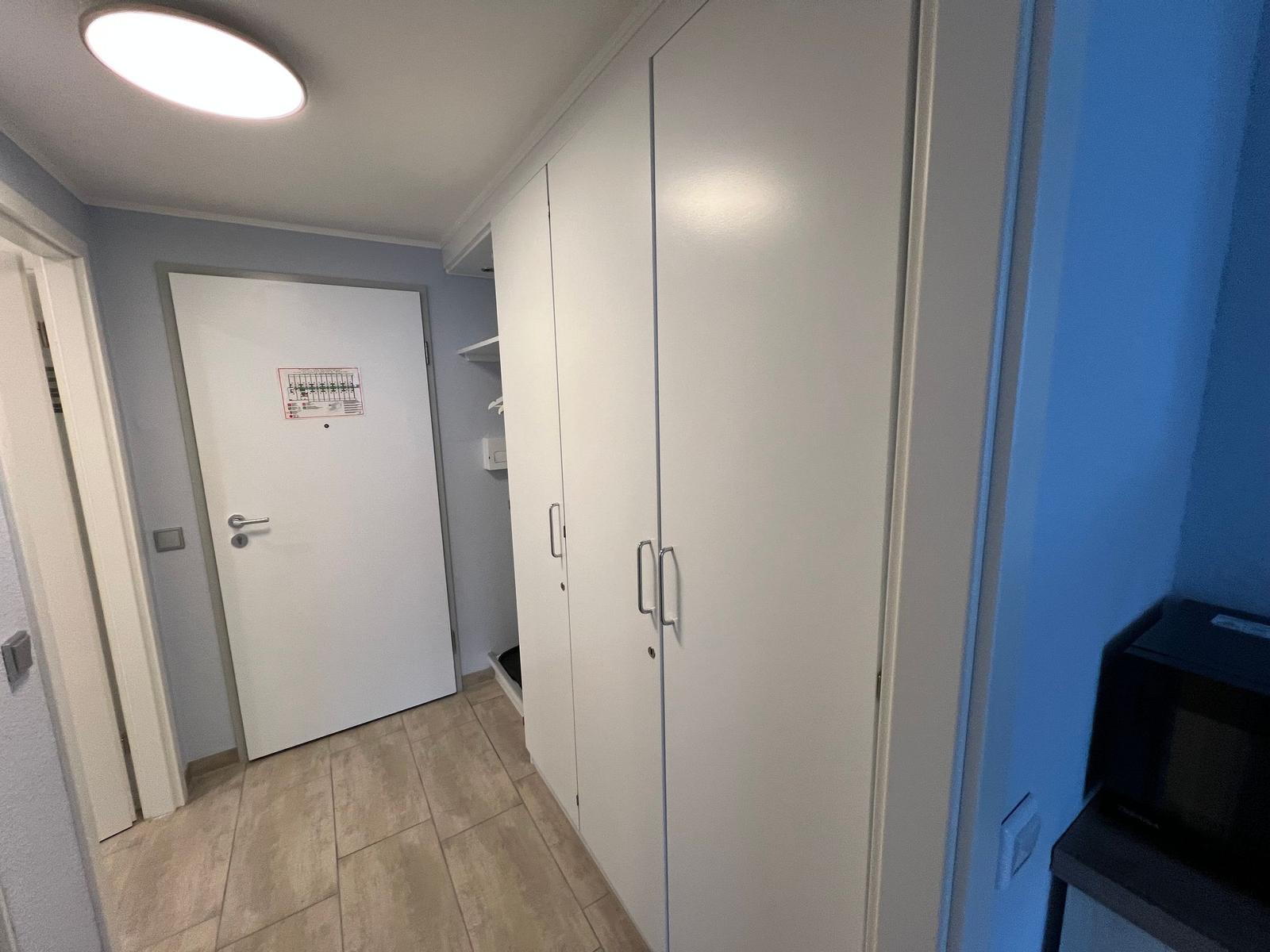 Flur mit weißen Schränken, Tür und Mikrowelle.