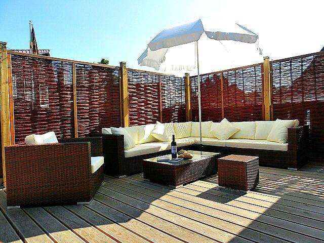 Terrasse mit Sitzgruppe, Sonnenschirm und Holzgeländer.