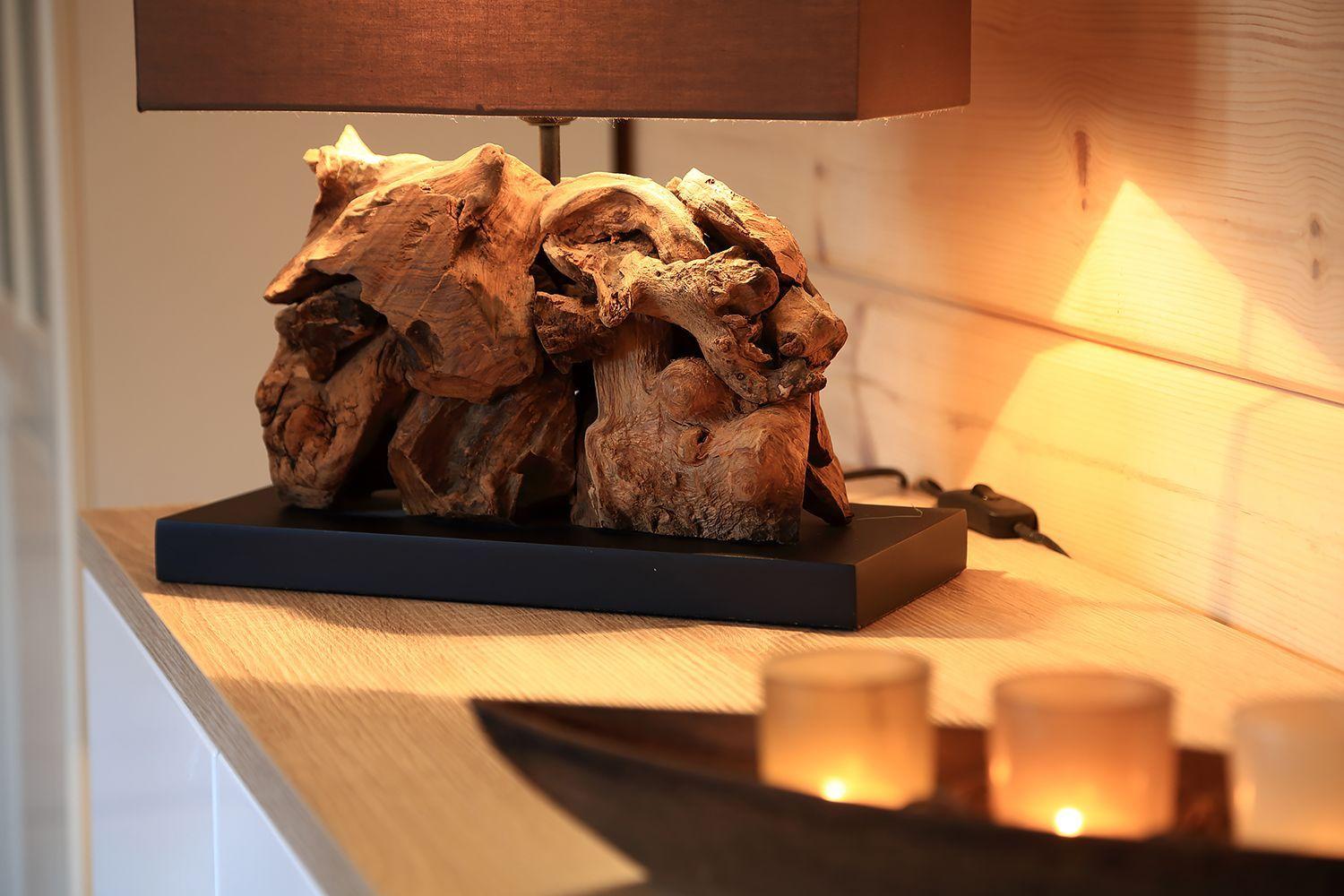 Tischlampe auf Holzsockel mit Holzdekoration und brennenden Kerzen auf Schreibtisch.