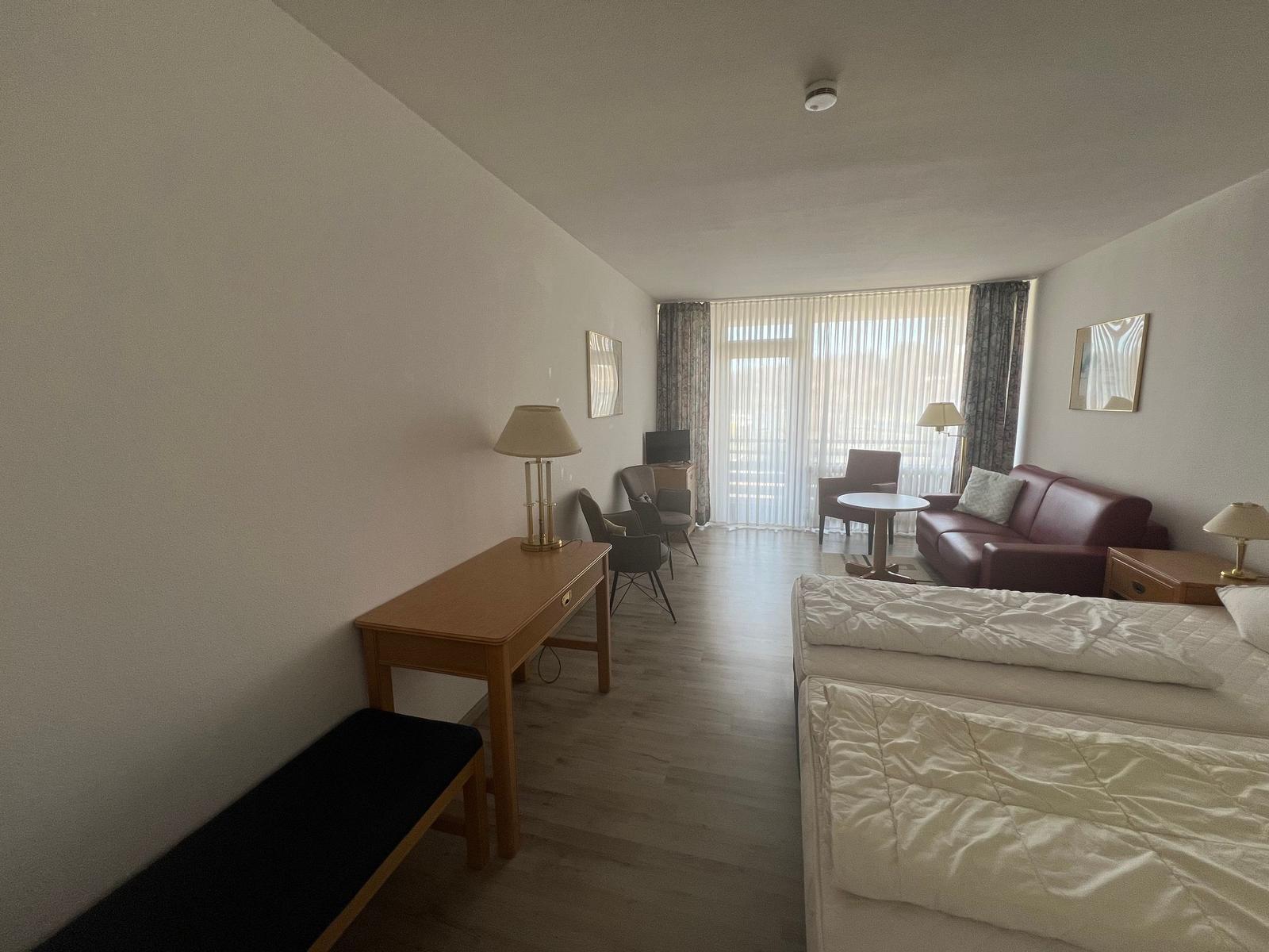 Ein Schlafzimmer mit einem Bett, einem Schreibtisch und einem Sofa. Durchgang zum Balkon mit Blick.