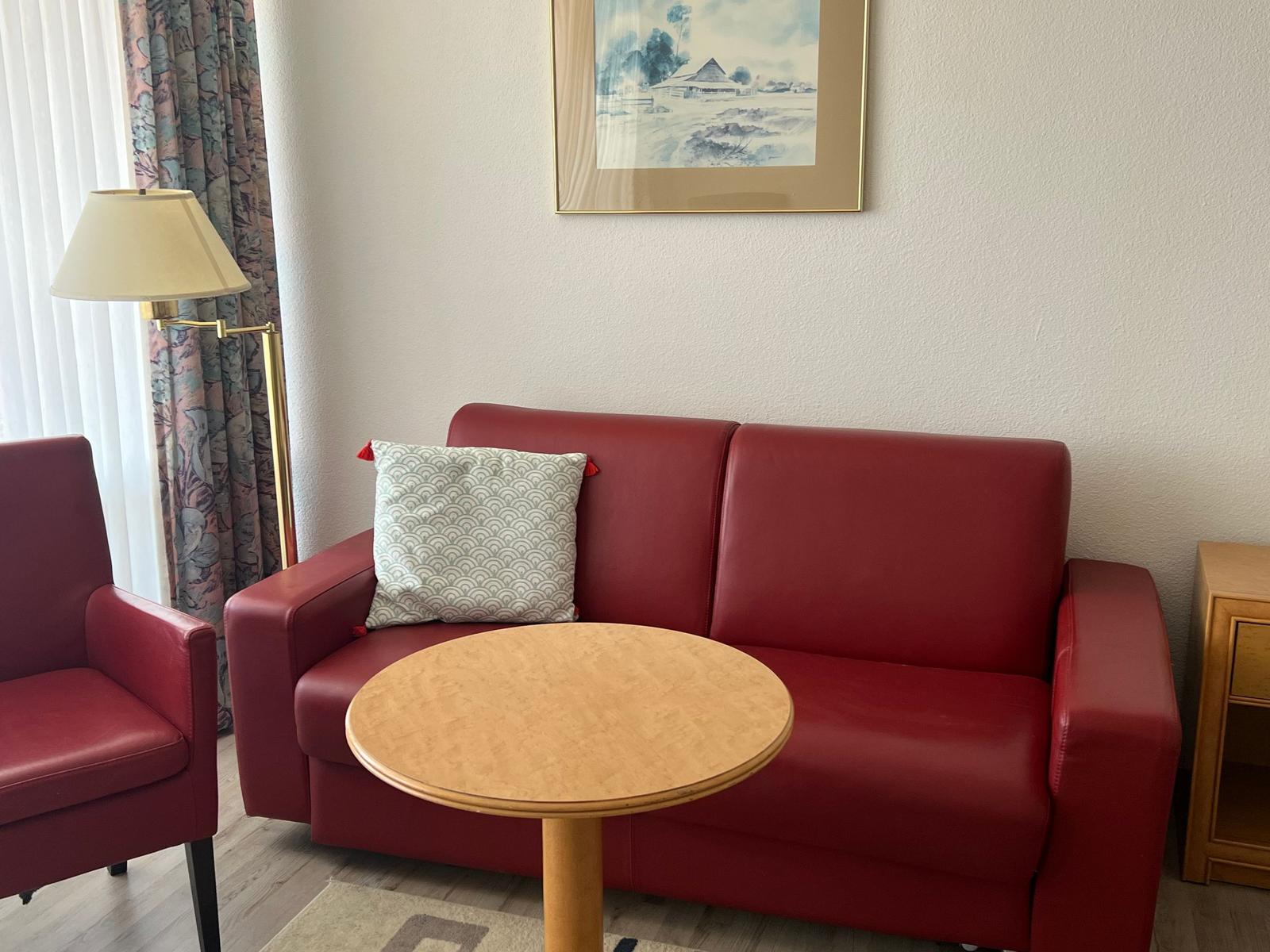 Ein Wohnzimmer mit rotem Sofa, runder Tisch und Stehlampe.