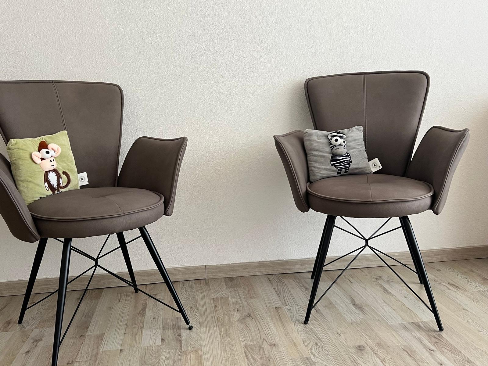 Zwei braune Sessel mit Kissen und Plüschtieren stehen auf Holzboden.