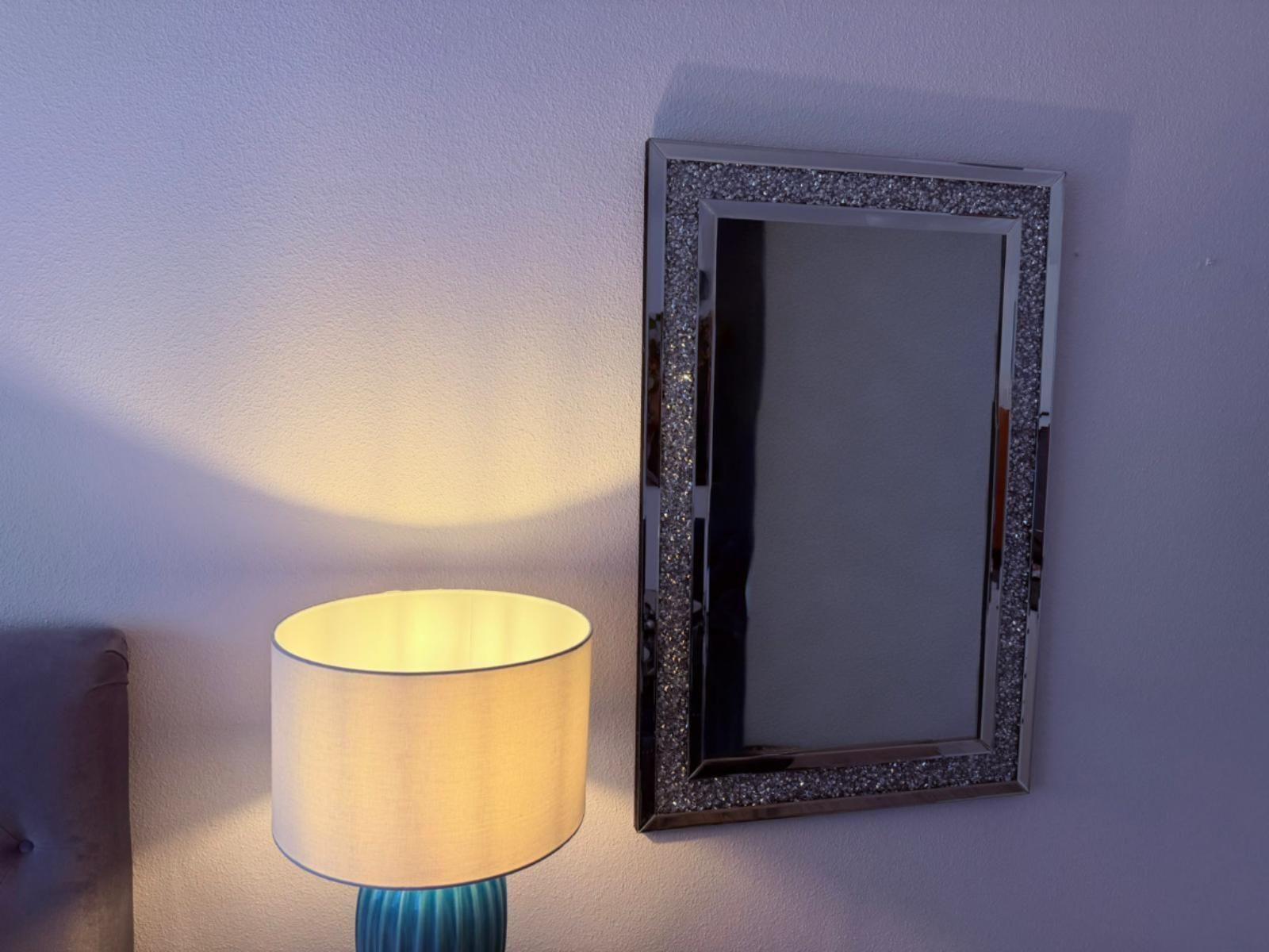 Lampe neben Spiegel an Wand. Spiegel hat glitzernden Rahmen.