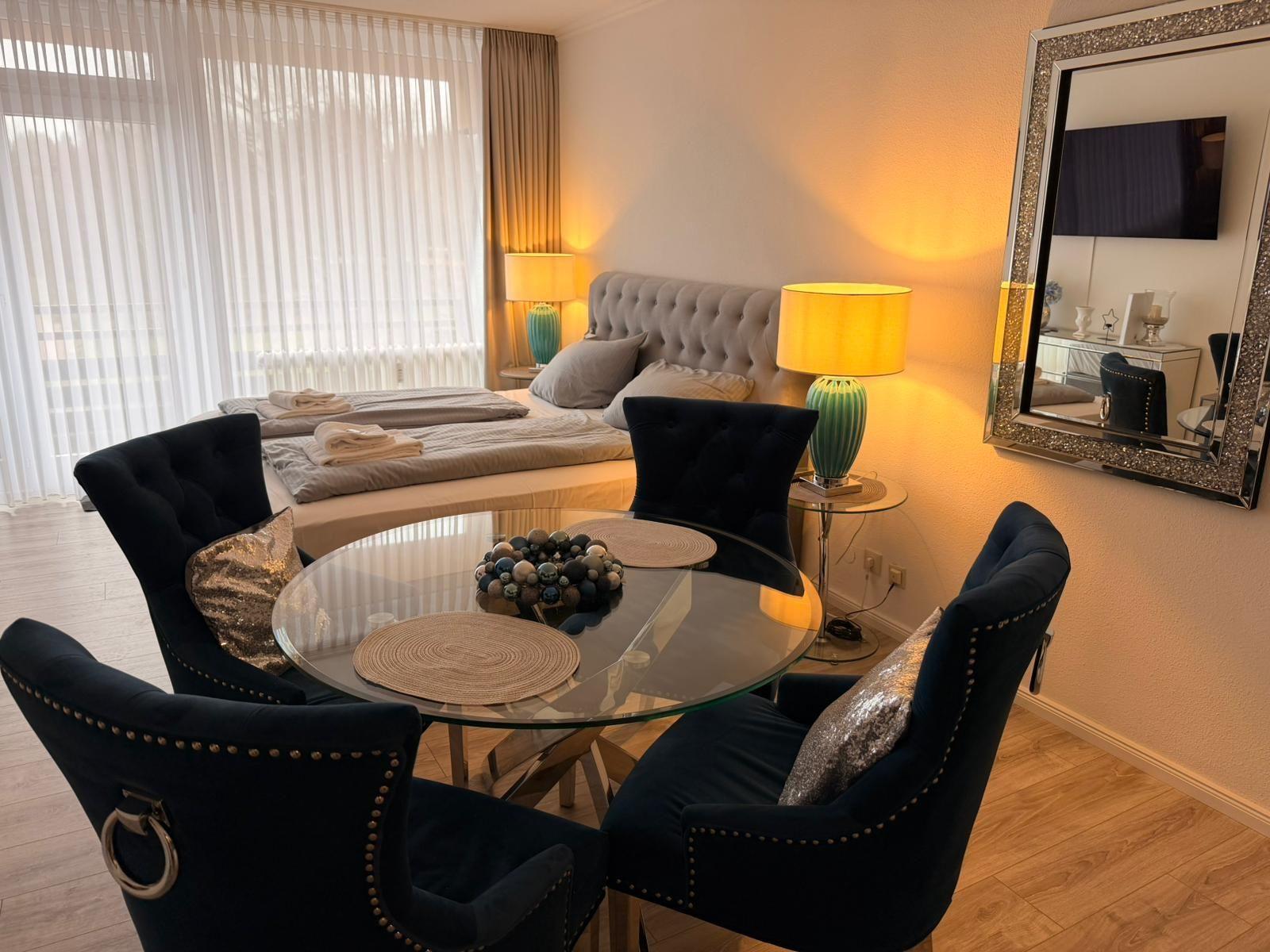 Ein Schlafzimmer mit einem Bett, einem runden Tisch und vier Stühlen. An der Wand hängt ein Spiegel.