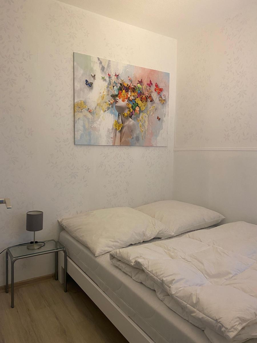 Ein Schlafzimmer mit weißem Bett, Nachttisch und Wandbild mit Schmetterlingen.