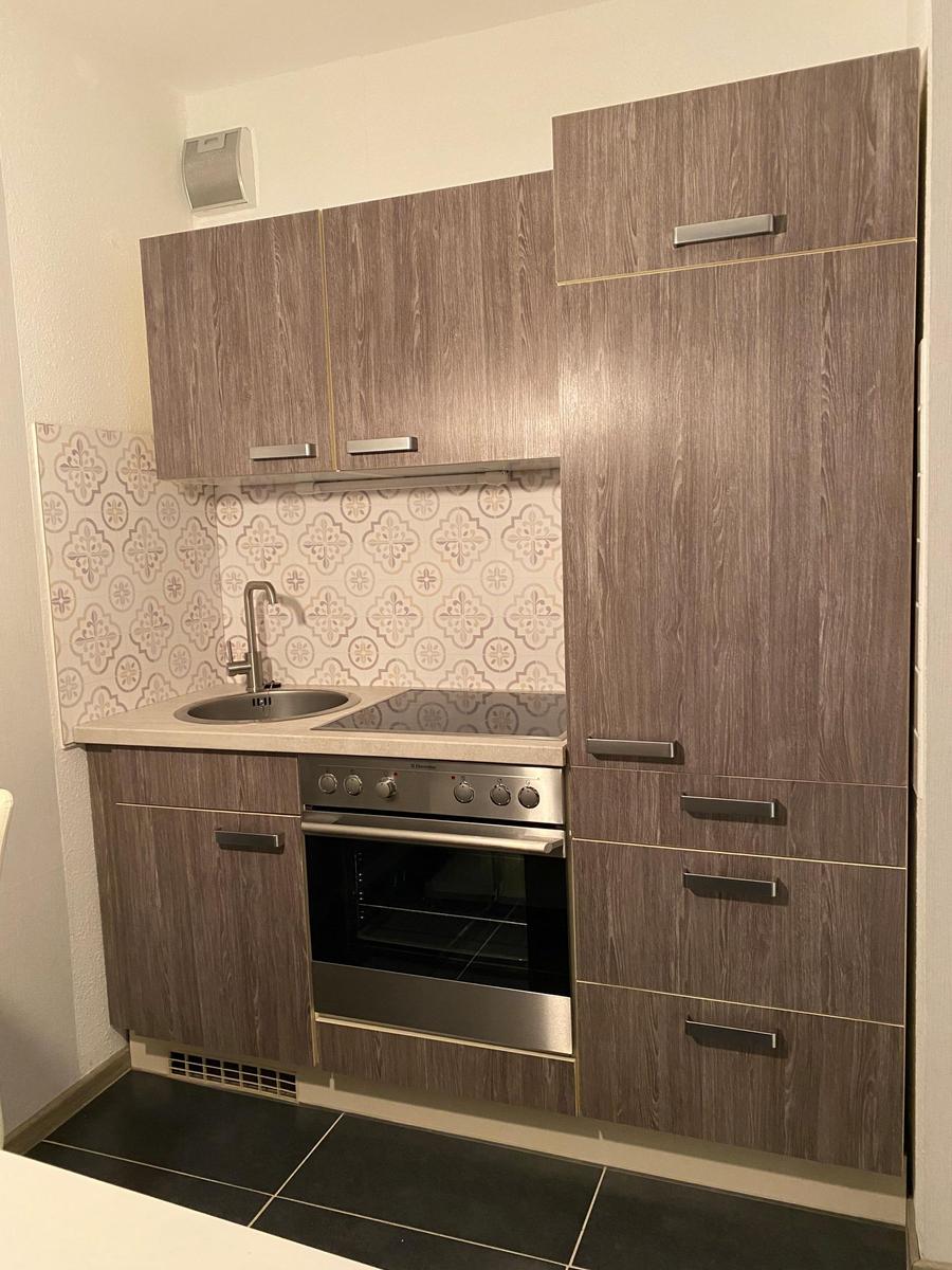 Küche mit Holzfronten, Spüle, Kochfeld und Ofen. Fliesenwand mit Muster.