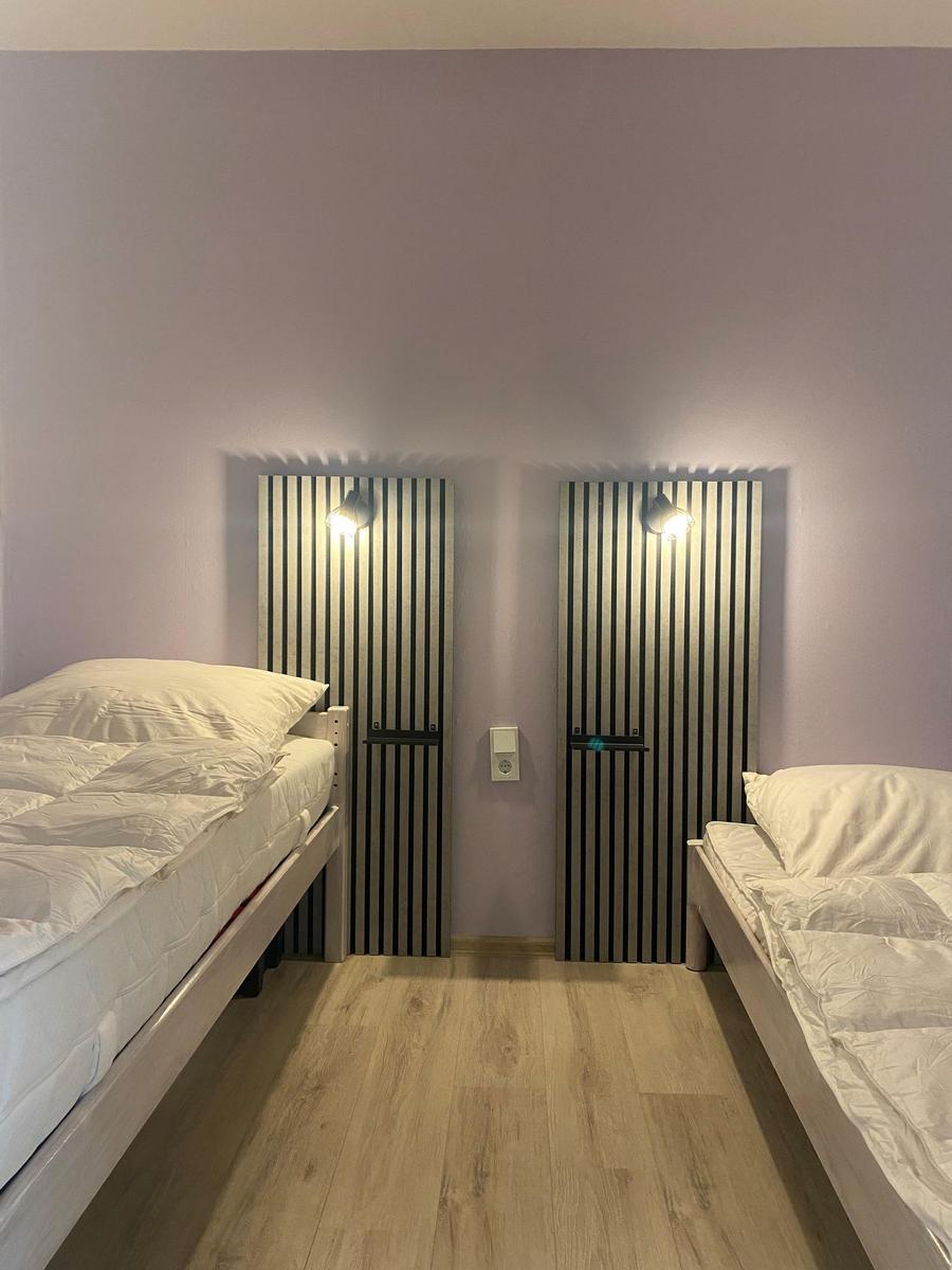 Zwei Einzelbetten mit weißen Bettwäschen stehen in einem Raum mit lila Wänden und Holzboden.