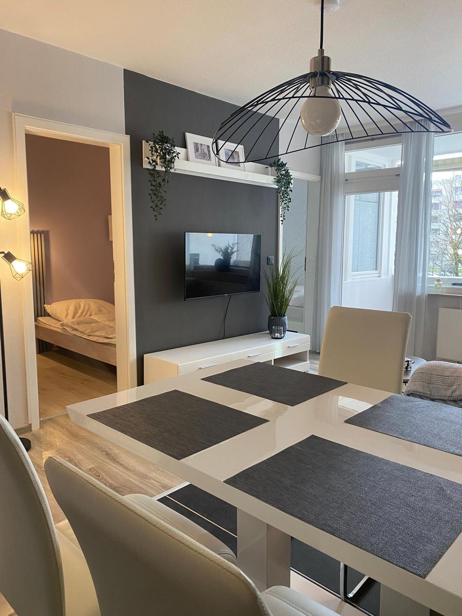 Essbereich mit Tisch und Stühlen, Fernseher an Wand, Blick in Schlafzimmer.