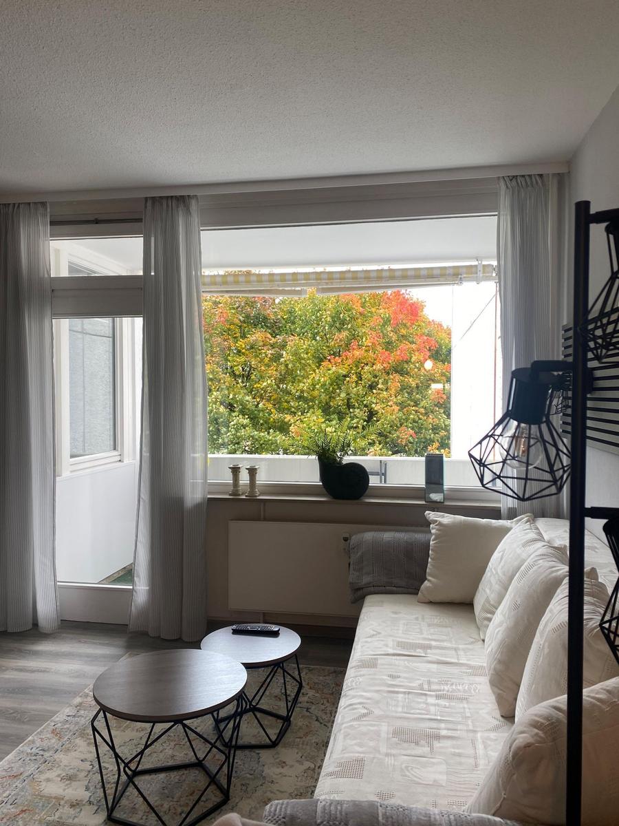 Wohnzimmer mit Sofa, zwei runden Tischen und Blick auf Bäume mit Herbstfarben.