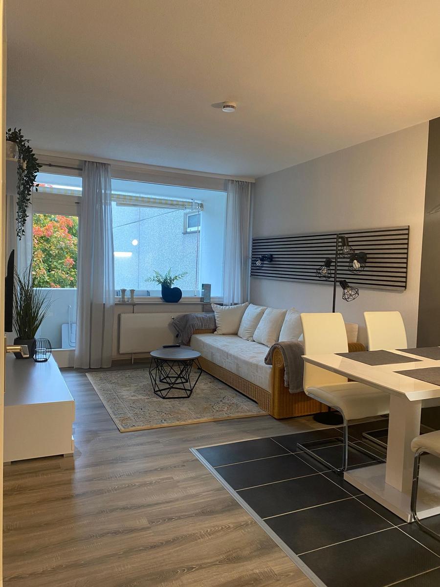 Wohn- und Essbereich mit Sofa, Tisch und Stühlen. Fenster mit Blick auf Balkon.