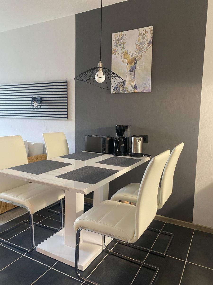 Essbereich mit weißem Tisch, weißen Stühlen und Dekorationsbild an der Wand.