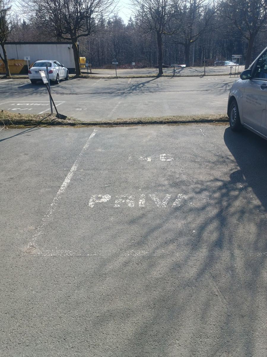 Privater Parkplatz mit markierten Stellplätzen und Bäumen im Hintergrund.