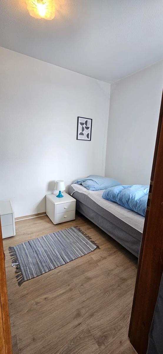 Schlafzimmer mit Bett, Nachttisch und Teppich auf Holzdielenboden.