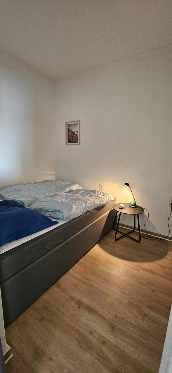 Schlafzimmer mit Bett, Nachttisch und Lampe. Holzdielenboden und Wandbild.